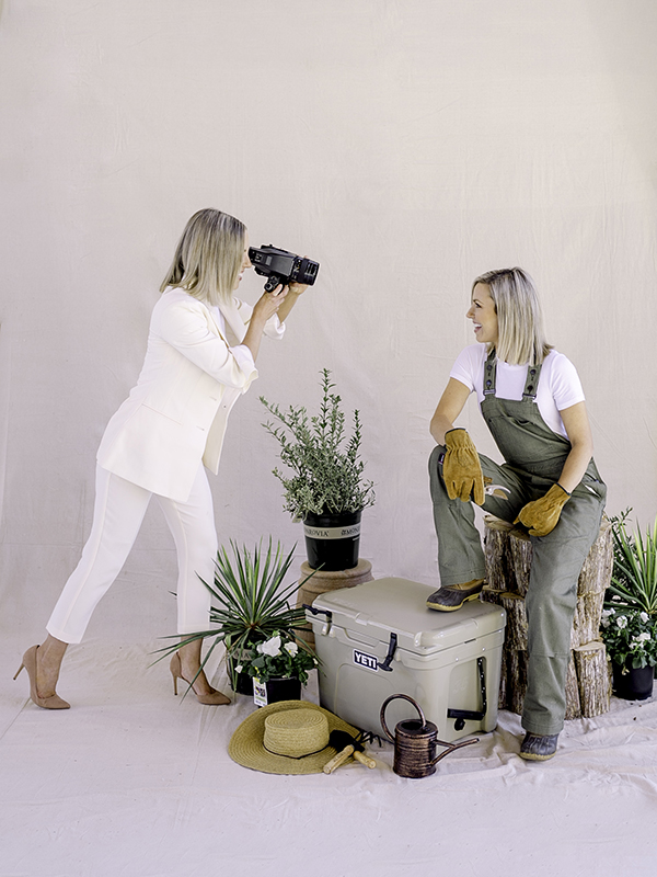 Those Plant Ladies: Heather photographing Fawn, surrounded by plants.