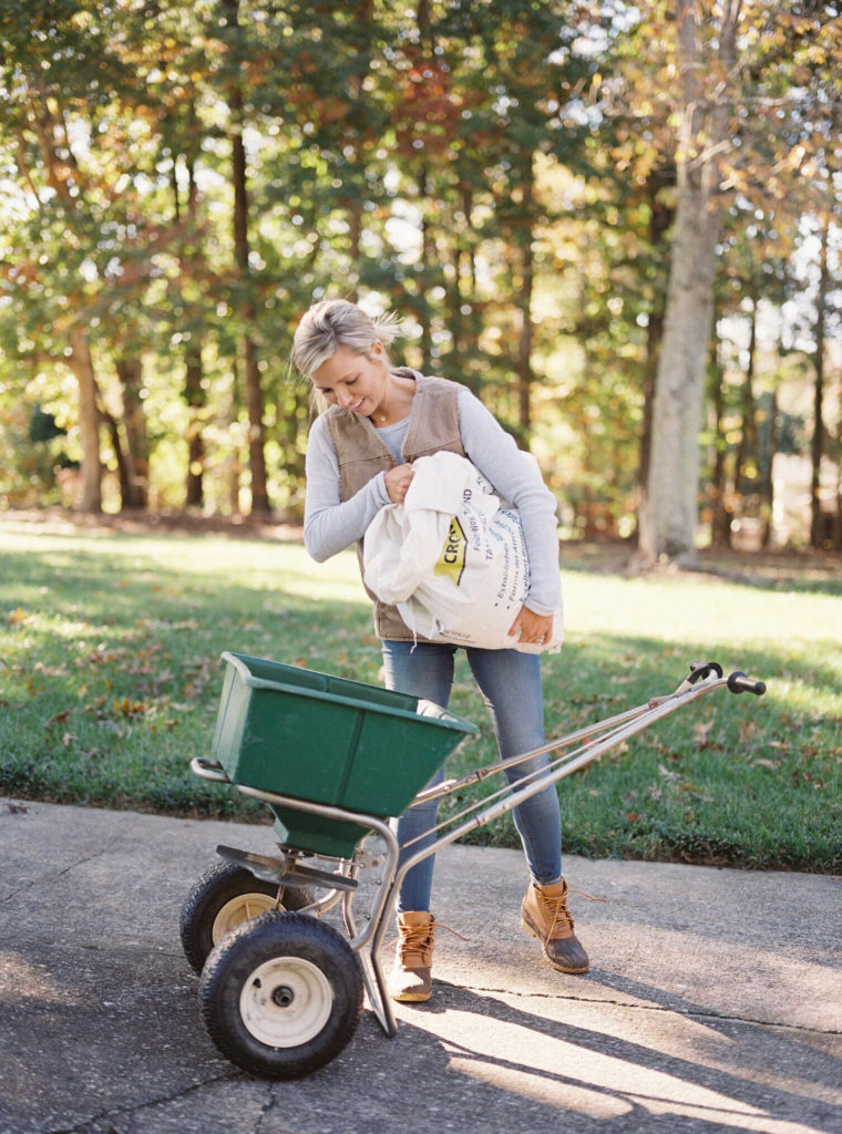 Woman pouring seed into a wheelbarrow outside.