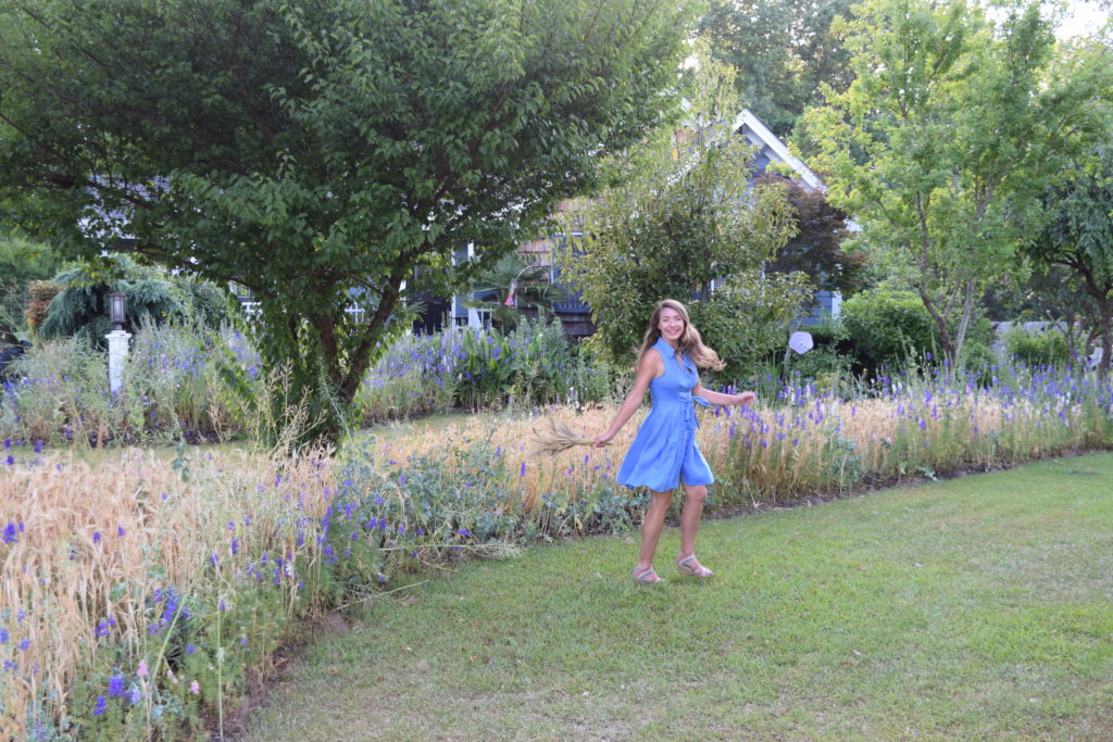 Brie Arthur dancing along the edge of a flower garden.