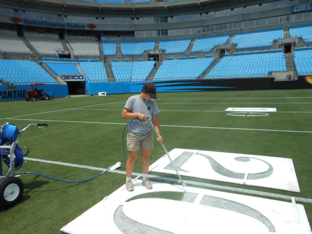 Alexa of Those Plant Ladies painting the 20-yard line at the Carolina Panthers' stadium.