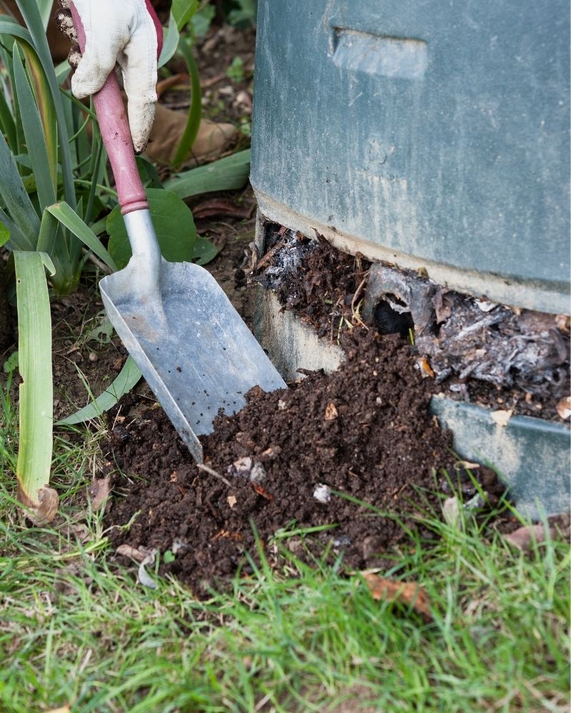 A metal compost bin with a shovel and composted dirt ready to use.