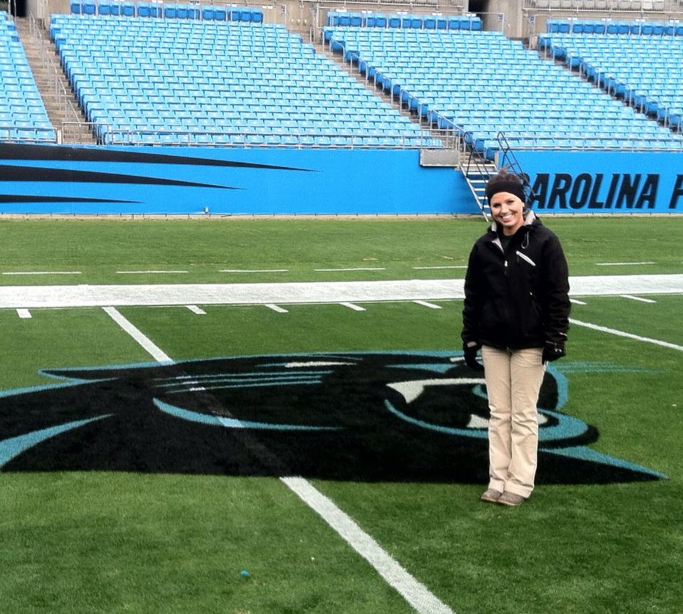 Fawn of Those Plant Ladies standing next to a Carolina Panthers logo she painted on the field.
