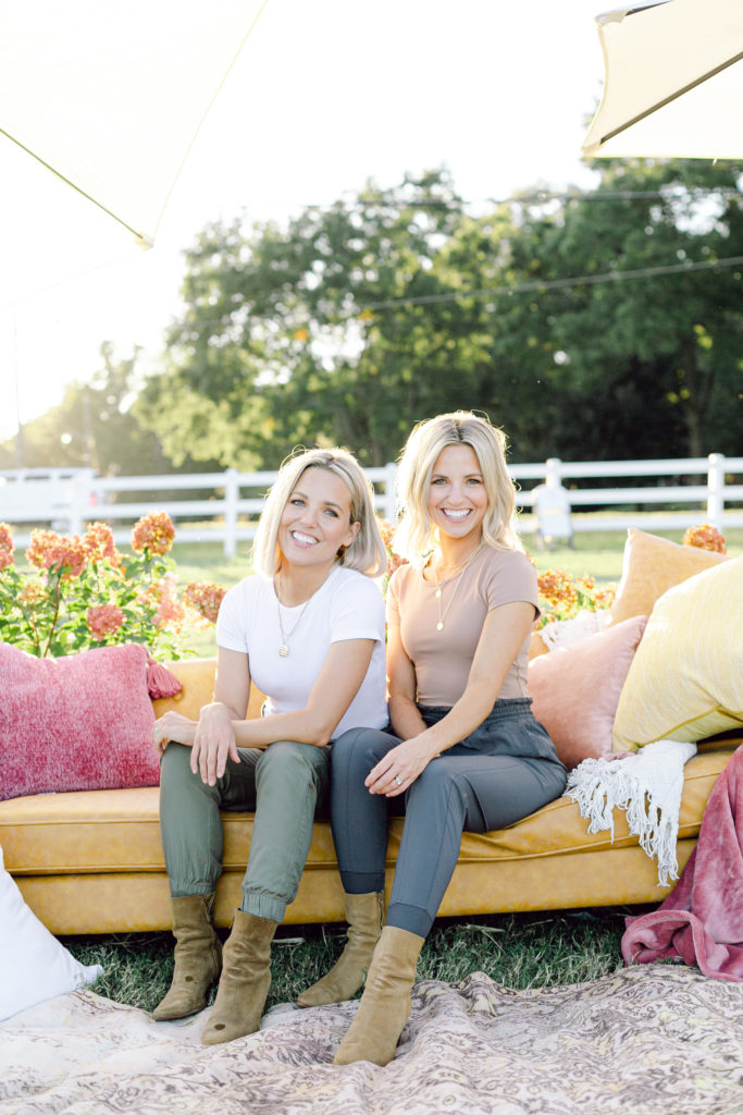Fawn and Heather of Those Plant Ladies sitting on a sofa, surrounded by pillows and flowers.