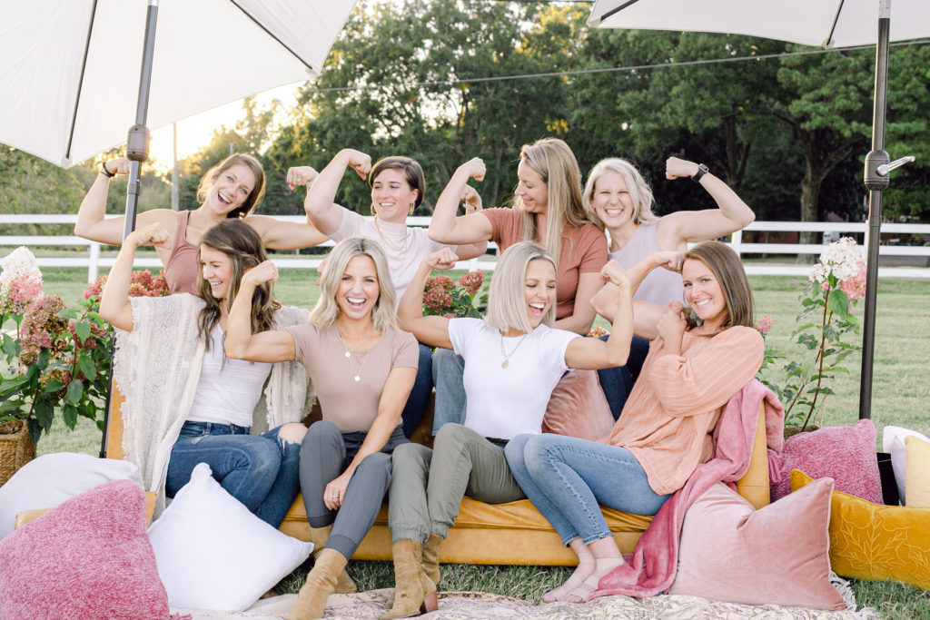 A group of women known as Those Plant Ladies sitting on a sofa outdoors and striking the muscle pose.