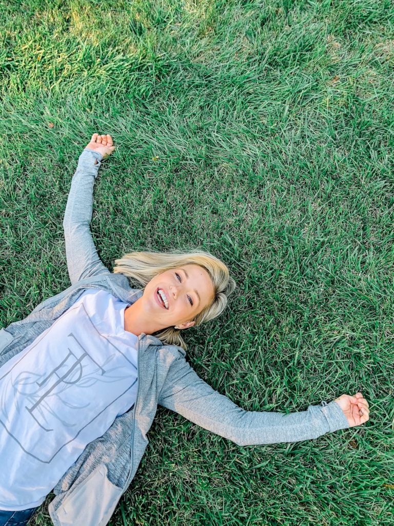 Fawn of Those Plant Ladies laying on grass with her arms spread wide.
